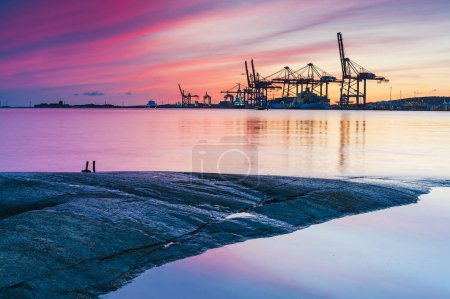 Photo for A commercial harbor at sunset: cargo containers, cranes, and a nautical vessel. - Royalty Free Image