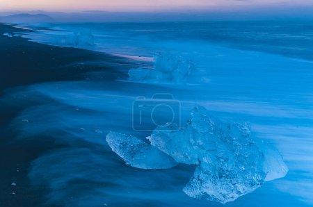 Foto de Un paisaje pintoresco de una playa islandesa al atardecer, con olas onduladas y nubes barridas por el viento que arrojan una hermosa luz sobre la costa helada. - Imagen libre de derechos