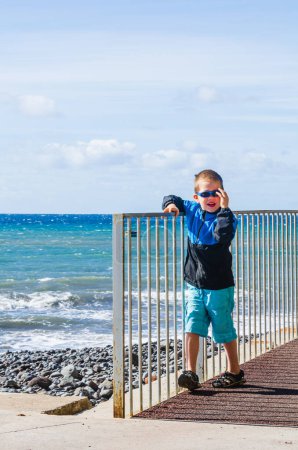 Foto de Niño con gafas de sol caminando junto al mar - Imagen libre de derechos