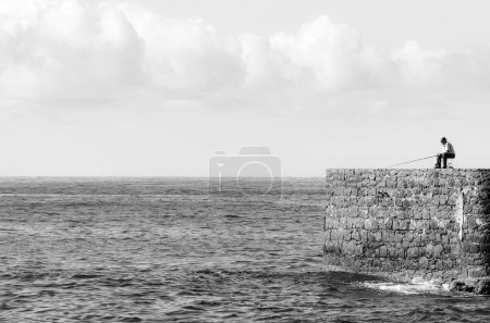 Photo for FUNCHAL, MADEIRA - NOVEMBER 11, 2011: Man fishing at end of pier - Royalty Free Image