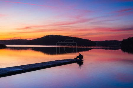 Téléchargez les photos : Homme assis sur la jetée au lever du soleil - en image libre de droit