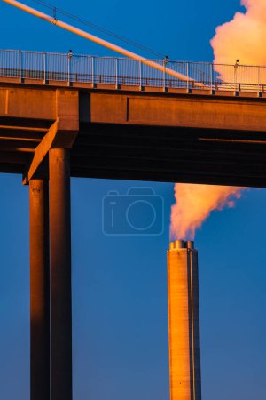 Photo for Industrial chimney by bridge billowing smoke into blue sky, low angle view, vertical image, Gothenburg, Sweden, Europe - Royalty Free Image