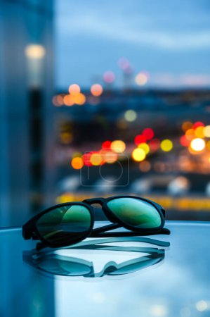 Photo for Sunglasses lying on table with blurred city in background. - Royalty Free Image