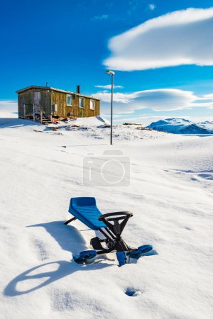 Snowracer in front of house in snowy Greenland under blue sky with sunlight