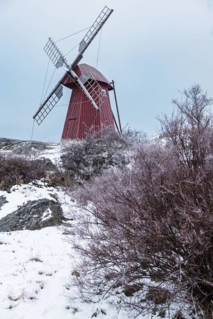 A red windmill stands prominently on a hill covered in pristine snow.