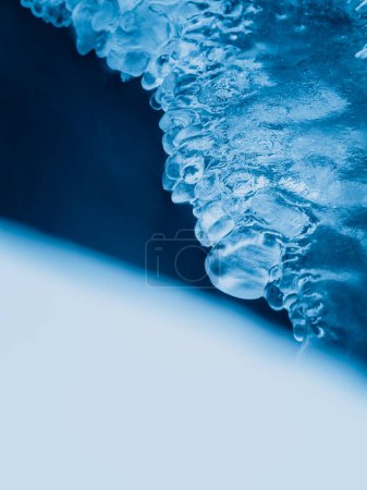 This image captures the intricate details of icicles clinging to a frozen edge, set against a soft, blurred blue background that accentuates the ices crystal-clear appearance.