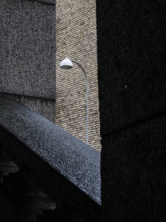 This image highlights the simplicity of urban design with a lone street lamp positioned between the converging angles of two buildings, partially obscured from view. The overcast sky suggests it may be an early morning or a cloudy afternoon.