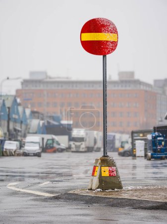 Das Bild zeigt ein knallrotes und gelbes No-Entry-Schild auf einer feuchten Stadtstraße mit sichtbaren Regentropfen oder Nebel. Die neblige Atmosphäre erzeugt eine Unschärfe um weit entfernte Fahrzeuge und Gebäude, was eingeschränkte Sichtverhältnisse impliziert..