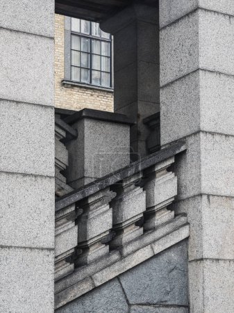 A unique view of a granite staircase juxtaposed against the external corner of a building, creating a visually striking geometric pattern. The staircase leads up to a classic window, and the gray tones of the stonework suggest an overcast day in Goth