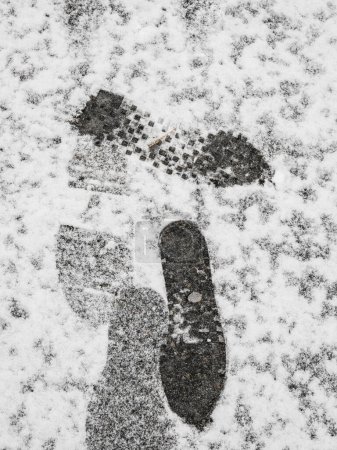 Foto de Un par de huellas dejan una marca en una manta de nieve recién caída que cubre una calle de Gotemburgo, capturando un momento solitario en un día de invierno. Las distintas formas de las bandas de rodadura de los zapatos están incrustadas en la fina capa de nieve, lo que ofrece una visión de - Imagen libre de derechos