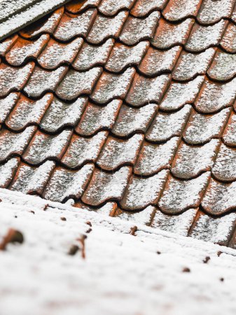 The rooftops of Gothenburg glisten as a fresh layer of snow covers the terracotta tiles, creating a stark contrast with its white dusting. The snowflakes have also lightly settled on the wooden surface in the foreground, indicating a recent snowfall 