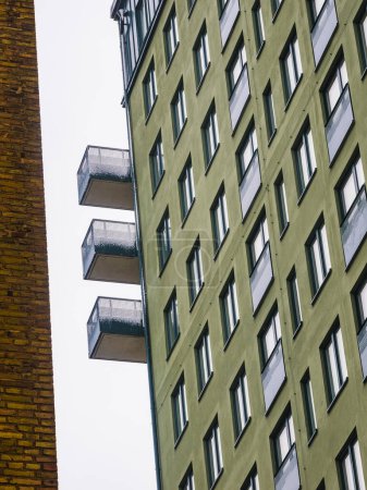 The facade of a contemporary building in Gothenburg is shown, featuring a sequence of balconies protruding against a gray sky. The buildings green exterior contrasts with the stark angles of the balconies, highlighting modern Swedish architecture on 