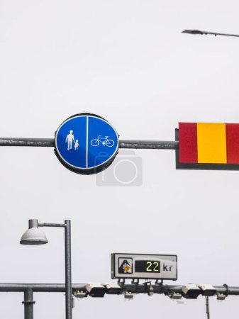 En un contexto de cielos nublados, una clara indicación para peatones y ciclistas se presenta junto a una barrera roja y amarilla, lo que sugiere una zona restringida en Gotemburgo, Suecia. A continuación, una farola cuelga silenciosamente, mientras que una etiqueta de precio que muestra 22