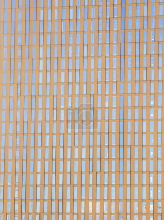 Foto de Una vista de cerca de un moderno edificio de oficinas en Gotemburgo, Suecia, mostrando un patrón simétrico de ventanas que reflejan el cielo azul. Los tonos dorados de los paneles exteriores de los edificios contrastan con el azul reflejado, demostrando una mezcla de urb - Imagen libre de derechos