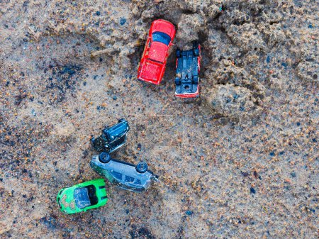 A variety of colorful toy cars is scattered over a gritty, sandy surface, suggesting playful activity. The shot, taken from above, captures the informal arrangement of the toys, possibly following a childs outdoor play session in Sweden.