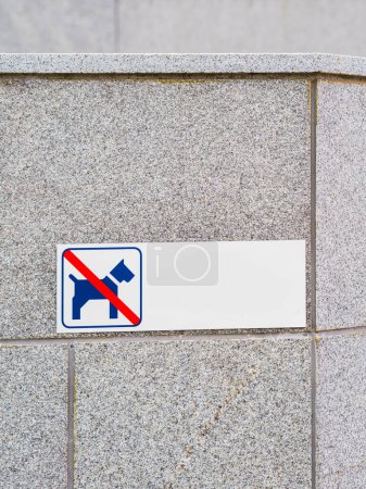 Ce panneau, fixé à un mur de pierre grise en Suède, indique clairement que la zone est interdite pour la promenade ou le repos des chiens. Le signe bleu et blanc présente le symbole universellement reconnu d'un chien dans un cercle rouge et une ligne diagonale indicati