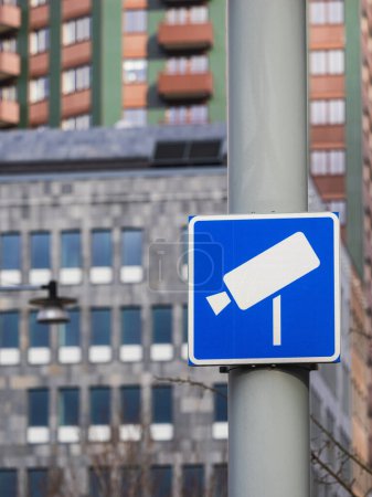 Un panneau de signalisation bleu orné d'une caméra de surveillance blanche se distingue par le paysage urbain animé de Gothenburg. Le panneau indique la présence d'un système de perception de péage surveillé par des caméras, une vue commune dans de nombreuses villes modernes. Dans le b