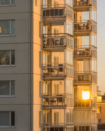 A tall residential building in Gothenburg, Sweden, featuring numerous balconies. The structure is illuminated by the warm hues of sunrise, creating a striking visual contrast.