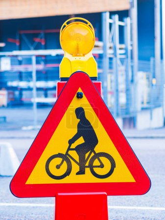 A yellow and red triangle warning sign is placed on the side of the road. The sign is likely there to caution cyclists of potential hazards ahead.