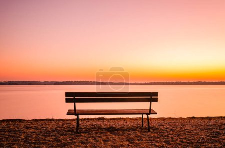 A lone bench offers a peaceful view across a calm lake beneath a colorful, dusky sky, reflecting the serene ambiance of a Swedish evening.