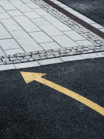 A freshly painted yellow arrow points right on the dark asphalt of a Swedish street, indicating the direction of traffic flow or guiding pedestrians.
