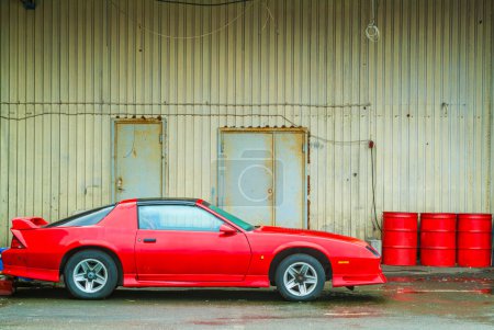 Red Sports Car Parked Beside a Rustic Metal Building on a Cloudy Day