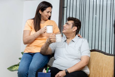 Photo for Happy Indian couple enjoying breakfast in bed and clinking coffee mugs while looking at each other with love, copy space - Royalty Free Image