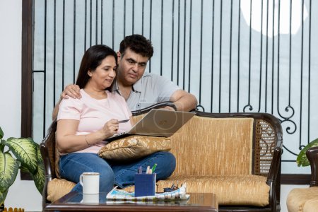 Photo for Portrait of young Indian happy cheerful family couple resting on sofa in living room searching internet typing online on laptop computer and speaking, choosing decor, e-commerce, leisure concept - Royalty Free Image