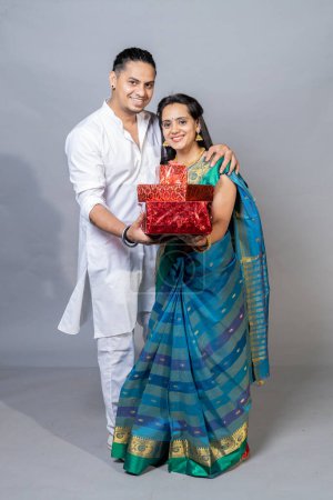 Téléchargez les photos : Portrait sur heureux jeune couple indien tenant boîte cadeau regardant vers l'appareil photo, concept d'offre festive Diwali - en image libre de droit