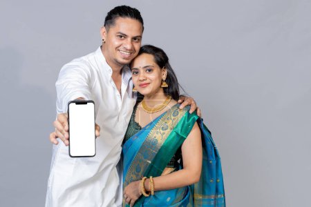 Photo for Indian Young couple in ethnic wear standing against grey background showing Phone blank screen towards the camera, - Royalty Free Image