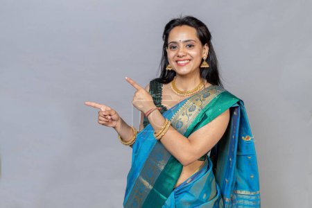 Photo for Portrait of Happy smiling Indian woman in saree looking towards the camera and pointing towards her left - Royalty Free Image
