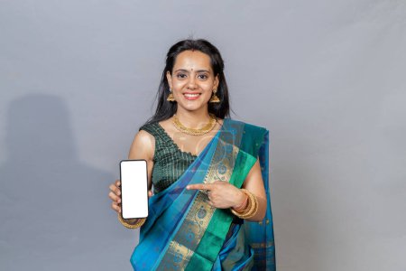 Photo for Indian woman in saree holding phone in hand looking towards the camera. Happy south Indian woman with phone looking towards the camera - Royalty Free Image