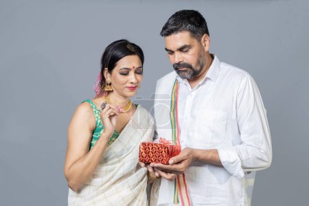 Photo for Portrait on south indian couple opening Gift box looking towards the camera - Royalty Free Image