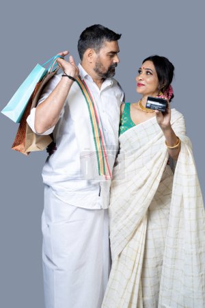 Téléchargez les photos : Couple indien en tenue ethnique avec sac à provisions et montrant carte de crédit vers l'appareil photo, concept shopping Festival - en image libre de droit