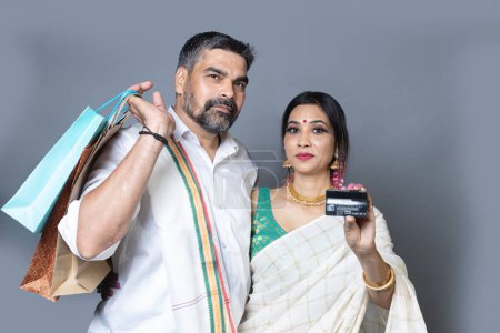 Téléchargez les photos : Couple indien en tenue ethnique avec sac à provisions et montrant carte de crédit vers l'appareil photo, concept shopping Festival - en image libre de droit