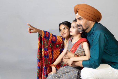 Photo for Portrait of Indian sikh Family together pointing towards the right .Lifestyle concept shoot of sikh family with copy space - Royalty Free Image
