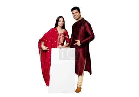 Photo for Indian couple holding white board, promoting offers on festival season while wearing traditional cloths, standing isolated over plain background - Royalty Free Image