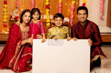 Photo for Portrait of indian Family indoor looking towards the camera with sign board ,Indian family in ethnic wear Advertisement festival concept - Royalty Free Image