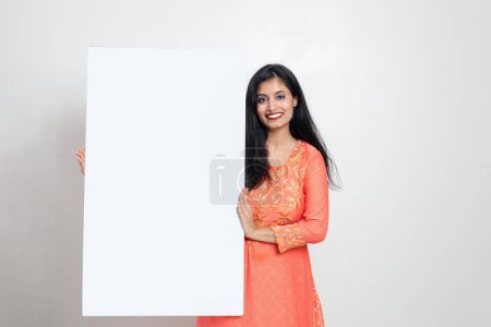 Photo for Indian woman in ethnic wear holding white sign board in hand and looking towards the camera , Advisement concept - Royalty Free Image