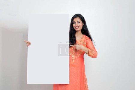 Photo for Indian woman in ethnic wear holding white sign board in hand and pointing towards it, Advisement concept - Royalty Free Image
