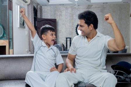 Photo for Indian Father and son in cricket dress watching cricket and supporting cricket team from home, Father son enjoying cricket - Royalty Free Image