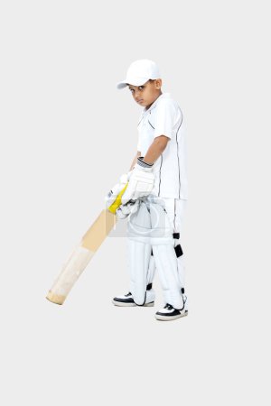 Photo for Full body portrait of indian kid in cricket dress holding cricket and ready for shot looking towards the camera on isolated background, cricket concept - Royalty Free Image