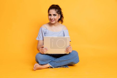 Photo for Young woman sitting isolated over yellow background using laptop computer. Looking camera - Royalty Free Image