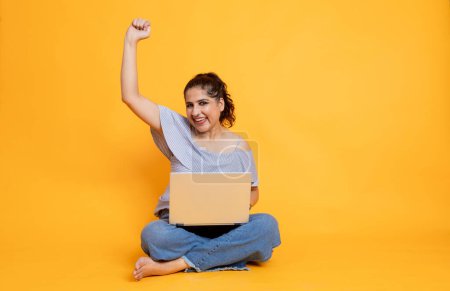 Photo for Portrait of attractive cheerful girl sitting in lotus pose using laptop on isolated over bright background, Female excited with offers and winning over internet - Royalty Free Image