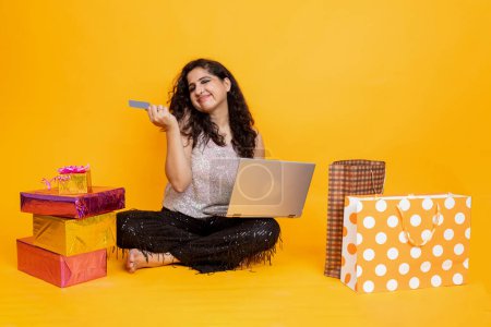 Photo for Indian girl sitting on floor with laptop doing online shopping from card, girl with laptop and gift box and shopping bag , online shopping concept - Royalty Free Image