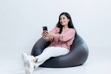Photo for Indian latin female sitting on bean bag and talking on Video call on isolated background - Royalty Free Image