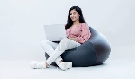 Photo for Indian female with laptop sitting on Bean bag on isolated white background and smiling - Royalty Free Image