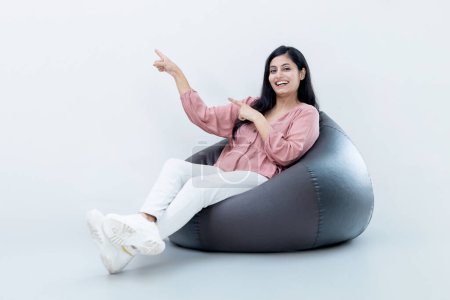 Photo for Indian latin Female sitting on bean bag pointing towards the empty space , Advertising concept - Royalty Free Image