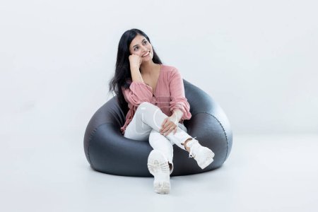 Photo for Indian latin Female sitting on bean bag and relaxing daydreaming on isolated background - Royalty Free Image