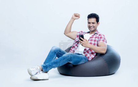 Photo for Excited man With mobile Sitting on bean bag looking in to Phone. Advertisement concept - Royalty Free Image